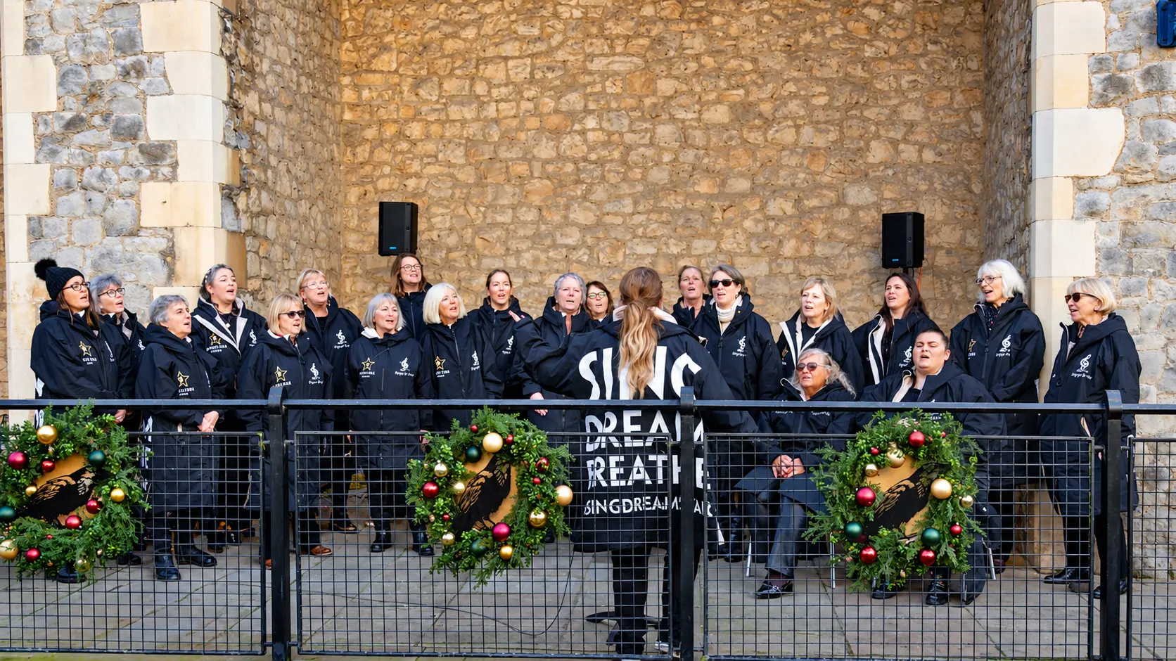 Ella conducting the choir in front of a stone wall decorated with Christmas wreaths