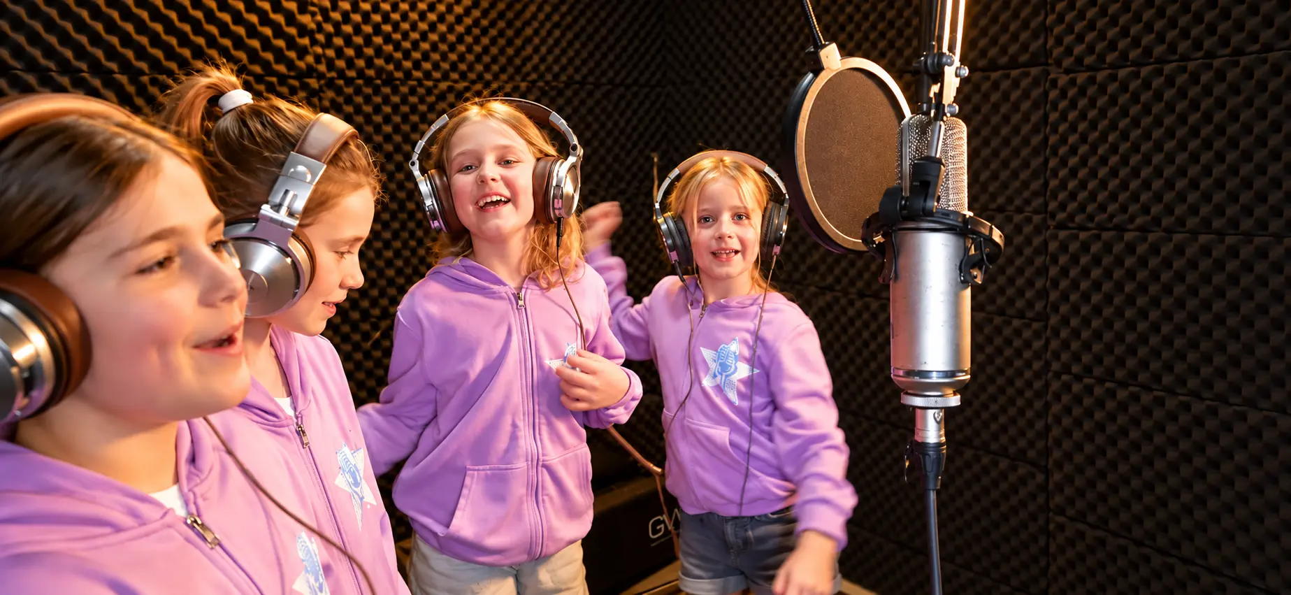 Four Rising Stars singers recording together around a studio microphone